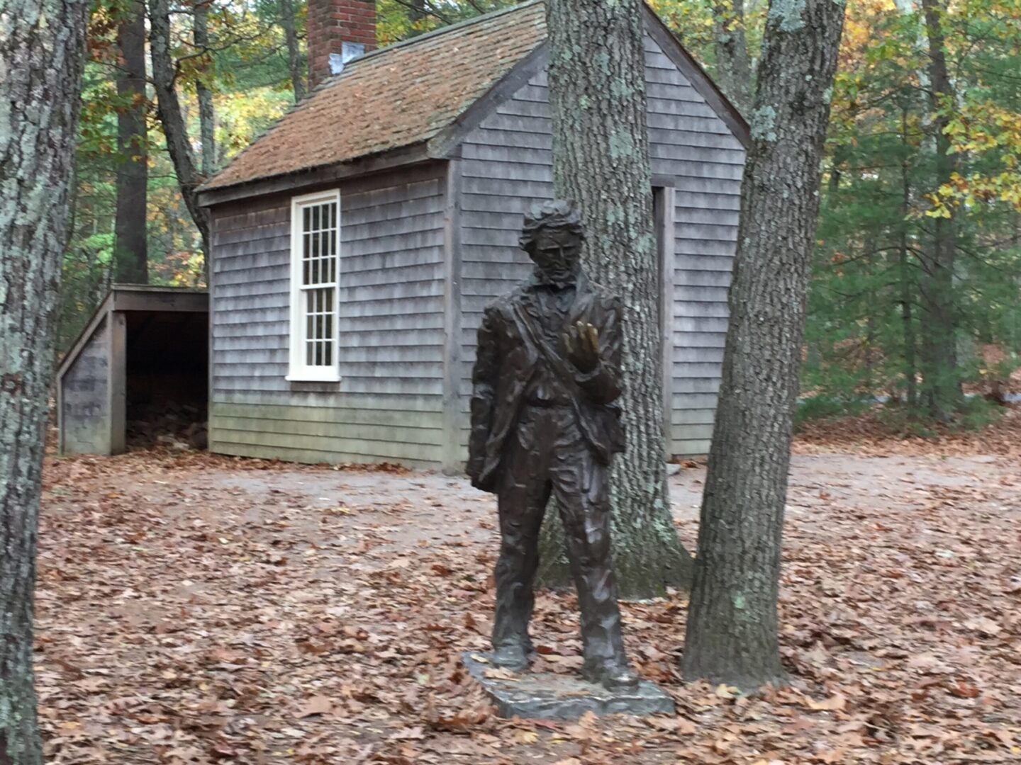 A statue of a man in front of a cabin.