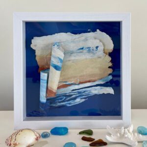 A framed piece of art with sea shells and sand.