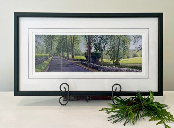 A framed print of a road with trees in the background.