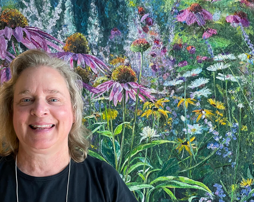 A woman smiles in front of a painting of wildflowers.