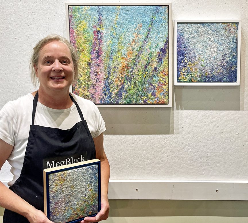 A woman holding a painting in front of a wall.