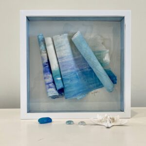 A white frame with blue and white paper and sea shells.