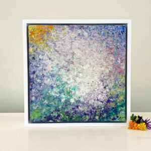 An abstract painting in a white frame on a table.