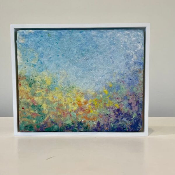 An abstract painting in a white frame on a table.