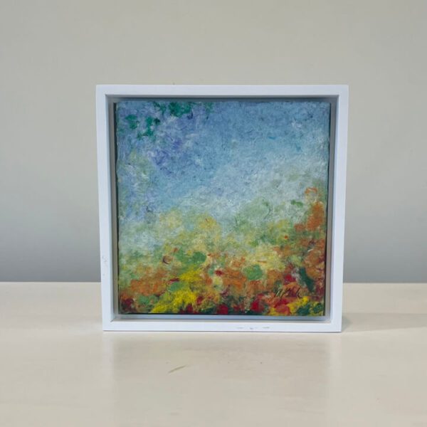 An abstract painting in a white frame on a table.