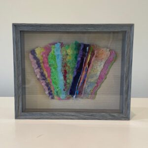 A framed piece of colorful paper in a wooden frame.