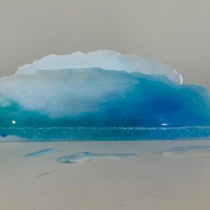 A resin art piece resembling a cross-section of the ocean, with varying shades of blue, displayed on a white surface.