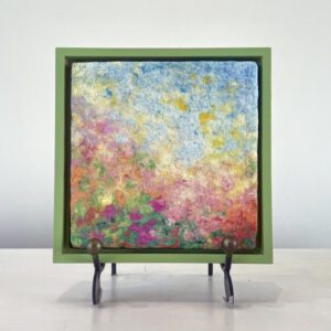 Colorful abstract painting displayed on a small easel with a green frame, set against a plain white background.