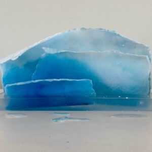 A translucent blue resin sculpture resembling layers of ice, displayed on a white surface against a neutral background.