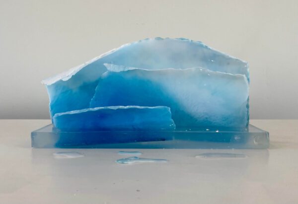 A translucent blue resin sculpture resembling layers of ice, displayed on a white surface against a neutral background.