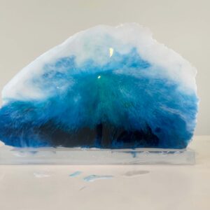 A translucent resin art piece resembling an ocean wave, displayed on a clear base, with gradients of blue and white colors.