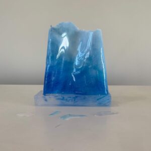 A translucent blue resin sculpture resembling an iceberg, displayed on a white surface against a neutral backdrop.