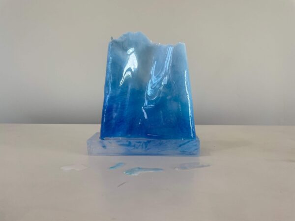 A translucent blue resin sculpture resembling an iceberg, displayed on a white surface against a neutral backdrop.