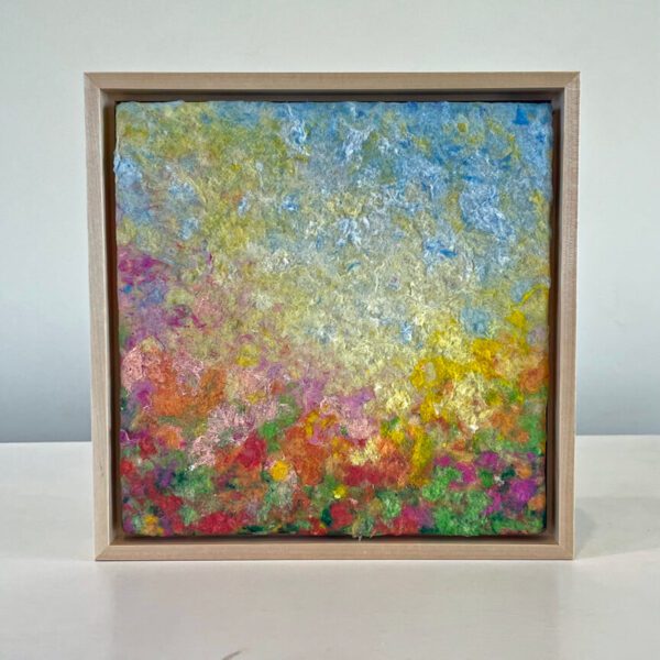 Abstract painting with vibrant splashes of yellow, blue, and pink colors, framed in a simple wooden frame, displayed against a white background.