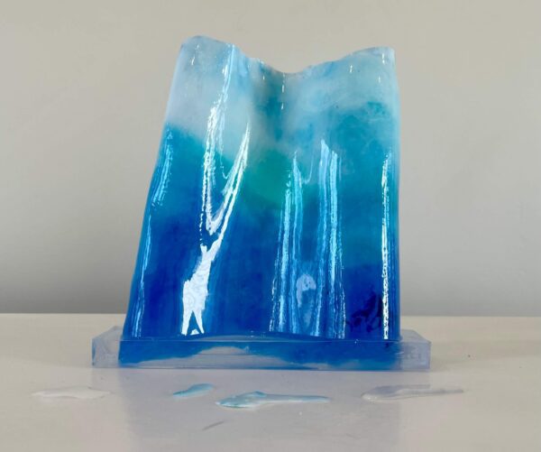A translucent blue sculpture reminiscent of a frozen waterfall, displayed on a white surface with small scattered shards.