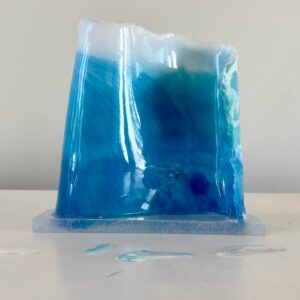 A blue resin art piece resembling a wave, displayed on a white surface.