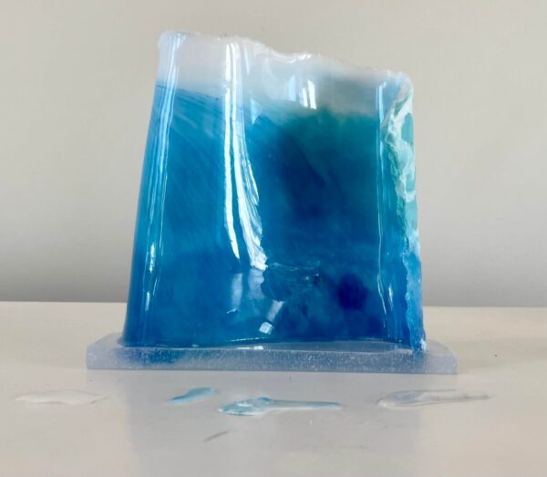 A blue resin art piece resembling a wave, displayed on a white surface.