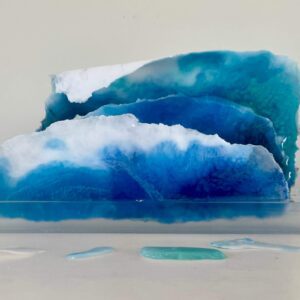 Three tiered resin art pieces showcasing layers of blue and white, resembling ocean waves, displayed against a plain background.