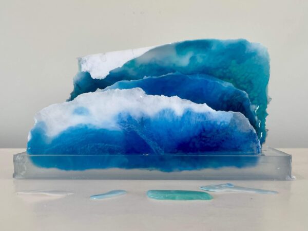 Three tiered resin art pieces showcasing layers of blue and white, resembling ocean waves, displayed against a plain background.