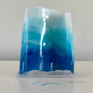 A translucent blue resin sculpture, resembling a block of ice, on a white surface against a plain background.