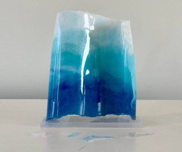 A translucent blue resin sculpture, resembling a block of ice, on a white surface against a plain background.