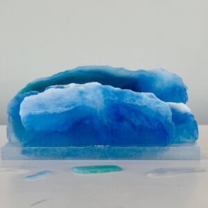 A translucent blue resin sculpture resembling layers of an iceberg, displayed on a neutral background with soft lighting.