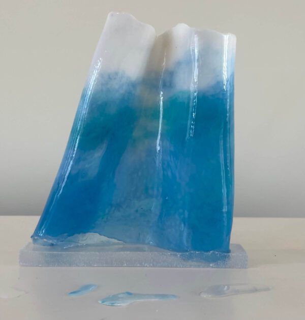 A translucent resin sculpture depicting an ocean wave, featuring gradients of blue on a white base, with drips on the surface below.